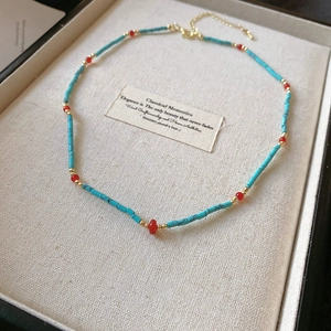 Close-up of bohemian beaded necklace with turquoise-style tubes and red spacers in a box