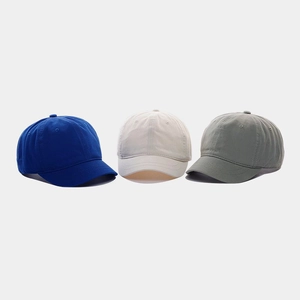 Dettaglio di tre cappellini da baseball in cotone con visiera corta in blu, beige e grigio