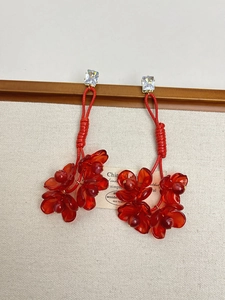 Macro view of long red acrylic floral tassel earrings with woven cord and zircon