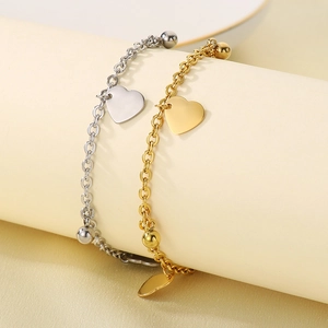 Eleganti cavigliere in acciaio oro e argento con ciondolo a cuore su piedistallo beige