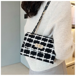 Close-up of black and white tweed crossbody bag with golden chain and square metal lock