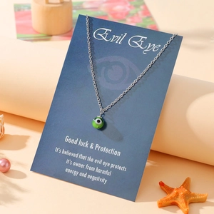Detail of green evil eye charm necklace on blue gift card with symbolic meaning