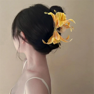 Detail of yellow-orange gradient lily flower hair claw clip worn on a woman's bun