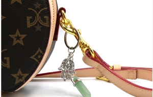 Detail of Hamsa hand charm and green crystal hexagonal pillar on a brown luxury bag