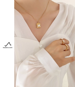 Golden stainless steel necklace with square pearl pendant and matching rings set on a model
