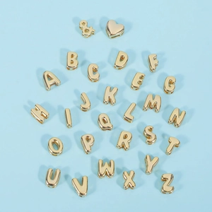 Detailed view of 18K gold bubble letter beads and heart charms on a blue background
