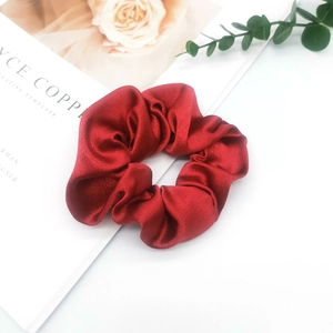 Detail of red satin scrunchie with soft folds and glossy texture on a minimalist background