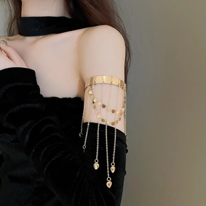 Macro shot of gold metal arm cuff featuring heart sequin tassels on a model with black velvet