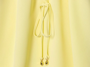 Detail van gele blouse met lantaarnmouwen en goudkleurige koordhanger