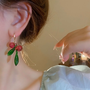 Close-up of cherry crystal drop earrings worn on ear with green leaves and gold hook
