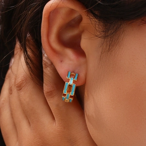 Close-up of sky blue enamel and 18K gold-plated chain earrings worn on ear