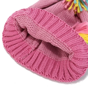 Close-up of pink thick knit children's beanie with colorful decorative pom-poms
