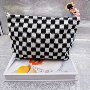 Detail of a large checkered knit cosmetic bag with a white zipper on a decorative book
