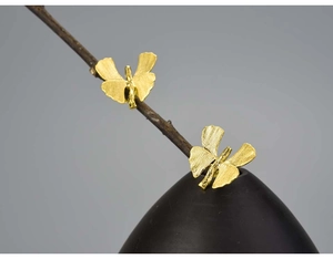 Artistic detail of gold ginkgo leaf and butterfly earrings on a rustic branch