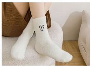 Detail of white plush crew socks featuring a small black embroidered heart on the ankle
