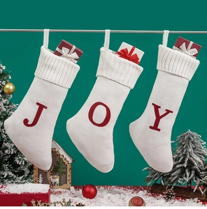 Close-up of three white knit Christmas stockings with red JOY letters on green background