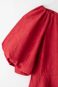 Détail de la robe rouge à manches bouffantes avec tissu texturé et froissé