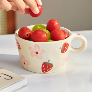 Detail of hand-painted strawberry ceramic mug filled with fresh fruits in hand