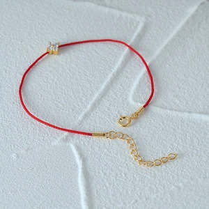 Detailed shot of a red string bracelet with a gold-plated clover pendant and crystals