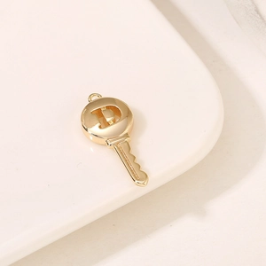 Macro view of gold key pendant with D-shaped hollow letter detailing for DIY jewelry