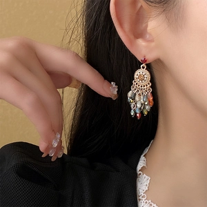Close-up of golden floral earrings with colorful crystal tassels on a model