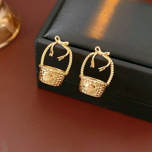 Macro detail of gold bow basket earrings showing woven texture on a black display stand