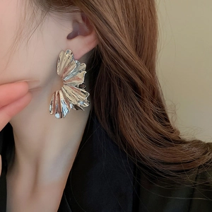 Detailed view of oversized wrinkled silver petal earrings on a model side profile