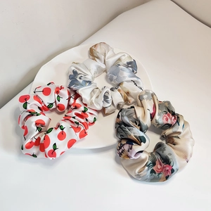 Three silk scrunchies with cherry and floral patterns on a white ceramic plate