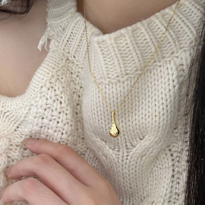 Detail of a minimalist gold teardrop pendant necklace worn over a cozy cream sweater
