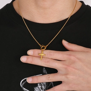 Close-up of golden cross necklace with OT toggle clasp on snake chain worn by model