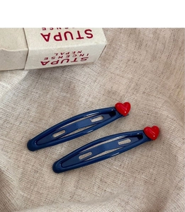 Detail view of two navy blue hair clips with red heart accents on soft linen fabric