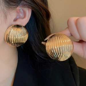 Macro detail of gold striped dome earrings featuring a textured metallic finish and round shape