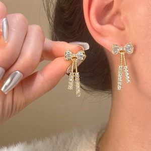 Detalle de pendientes de lazo dorado con borlas de cristal usados para mostrar el tamaño
