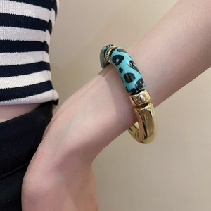 Détail d'un bracelet gourmette en acrylique doré avec motif léopard vert sur le poignet