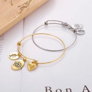Close-up of gold and silver adjustable bracelets with lotus and heart charms on wood
