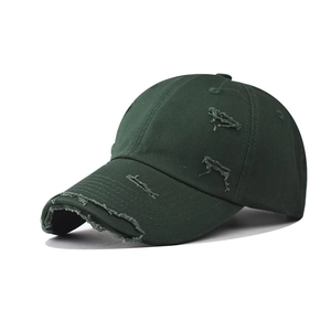 Close-up of distressed dark green baseball cap with frayed holes and vintage washed texture