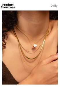 Detail of 18K gold-plated triple snake chain with a white heart charm on a model