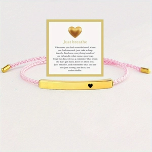 Detailed shot of pink woven bracelet with 'Just breathe' engraved golden tube on a card