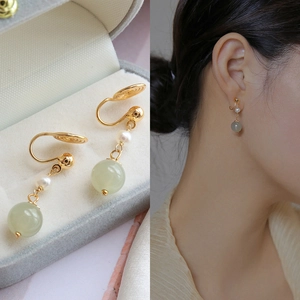 Detail of clip-on earrings with white pearl and green jade bead on gold metal clip