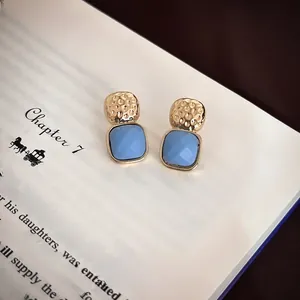 Close-up of blue square gemstone earrings with hammered gold metal on vintage book pages