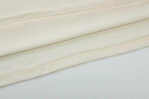 Close-up of double-stitched hem on cream-white fabric for summer two-piece sets