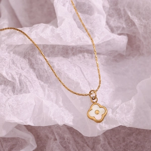 18K gold plated clover necklace with white shell pendant on a textured white background