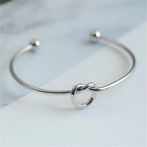 Close-up of a silver minimalist open cuff bracelet with a central knot design and ball ends
