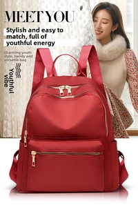 Detail view of red Oxford cloth backpack featuring multi-zipper pockets and gold hardware