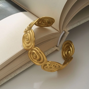 Detailed close-up of golden spiral relief texture on a wide open stainless steel bangle