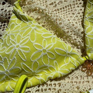 Detail of neon green bikini top with daisy embroidery and gold floral charm accessory
