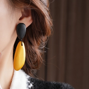 Detail of geometric teardrop earrings featuring a black pebble and yellow pendant on a model