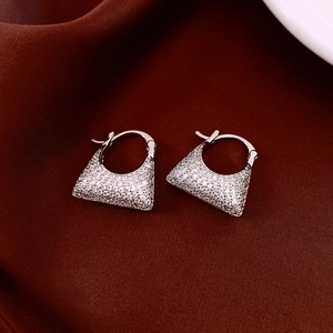 Macro shot of silver zircon bag-shaped earrings on dark red silk background