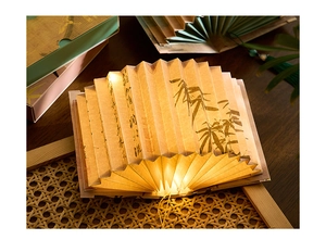 Macro view of folding book lamp featuring ink bamboo art and warm yellow LED light glow