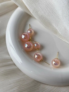 Close-up of pink mermaid pearl stud earrings on a white porcelain plate background